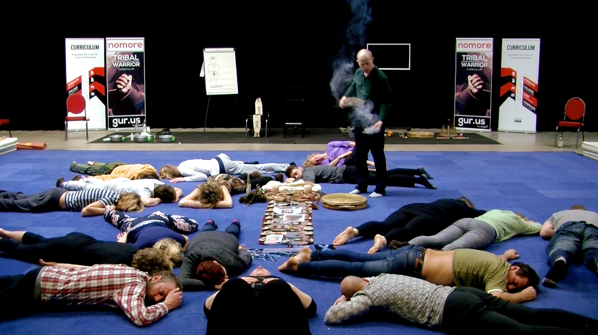 Coen smudge-cleansing a large group lying face down in a Tribal Warrior curriculum session